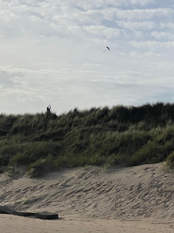 man flying a kite over sand dunes